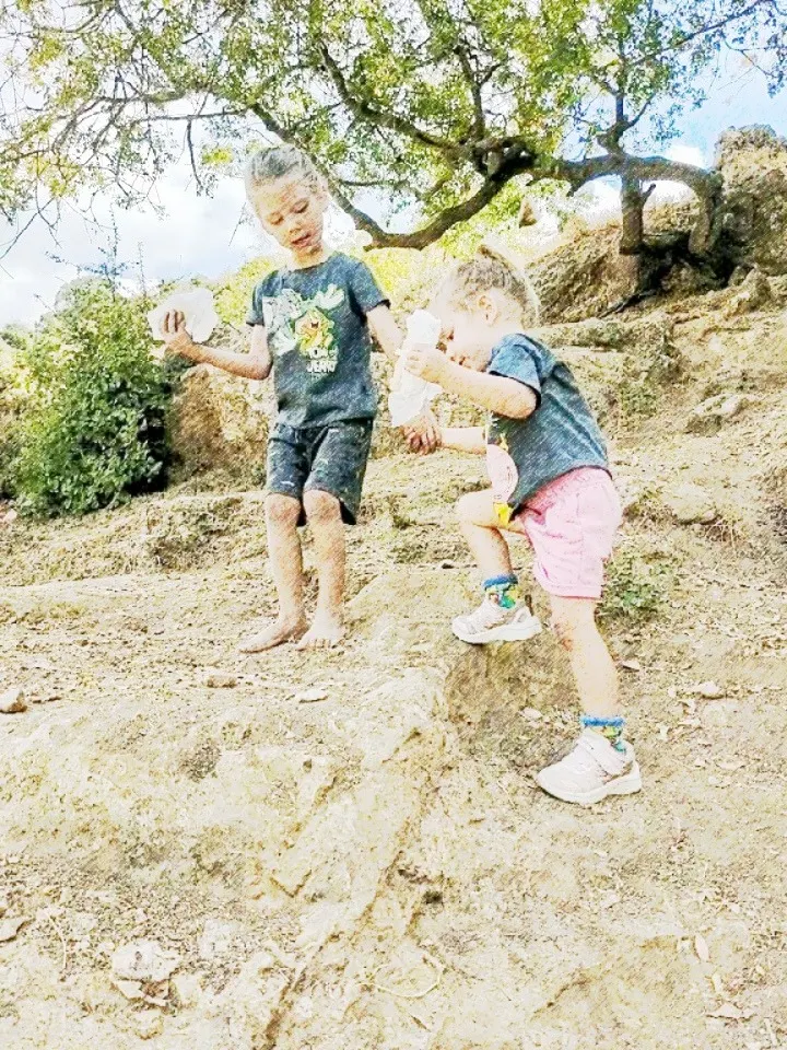 שני ילדים קטנים מטפסים יחד על סלע, מחזיקים ידיים